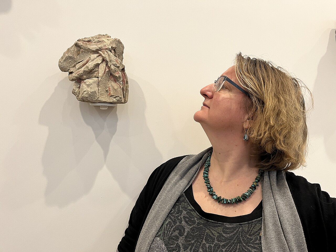 Porträt von Daniela Nicklas, sie blickt links neben sich auf eine abstrakte Skulptur an der Wand.