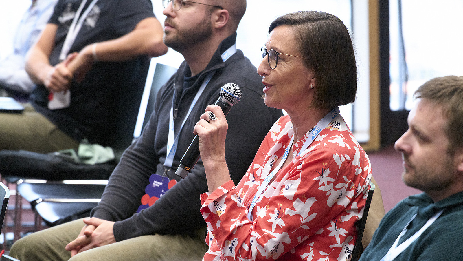 Blick ins Publikum der Konferenz, Manuela Urban hält ein Mikro und stellt eine Frage an die Menschen auf der Bühne
