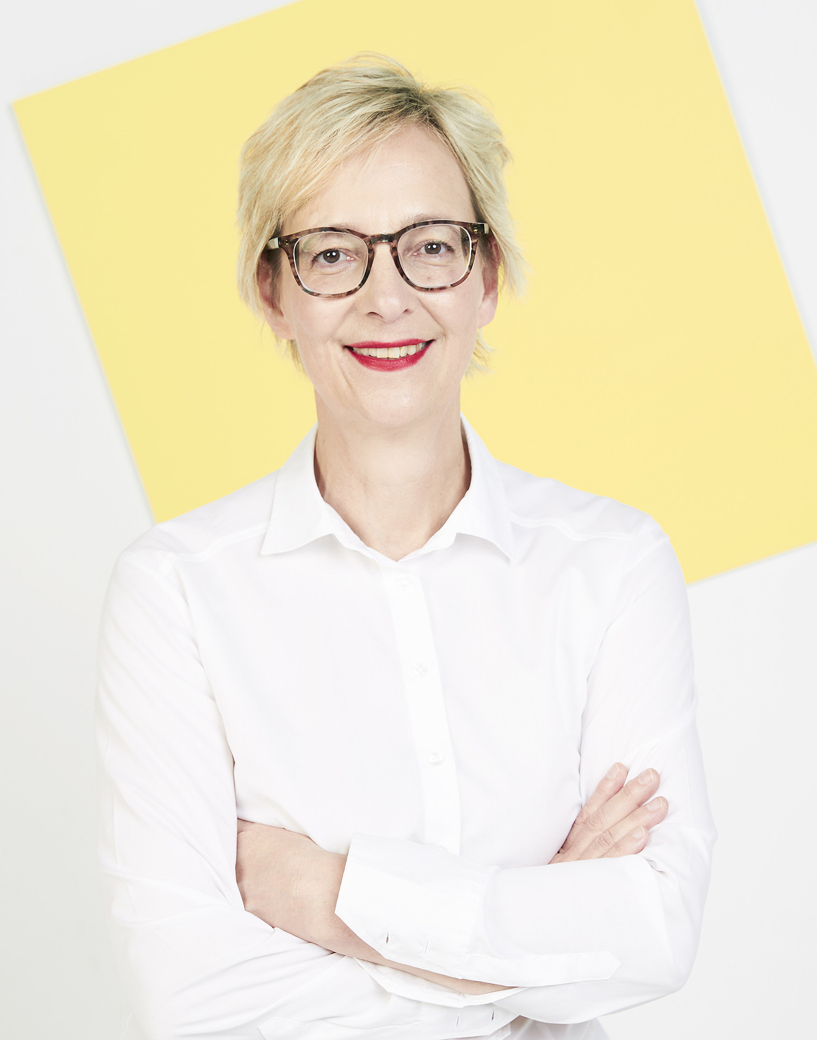 Portrait von Christine Regitz auf weißen Hintergrund mit gelber Kachel