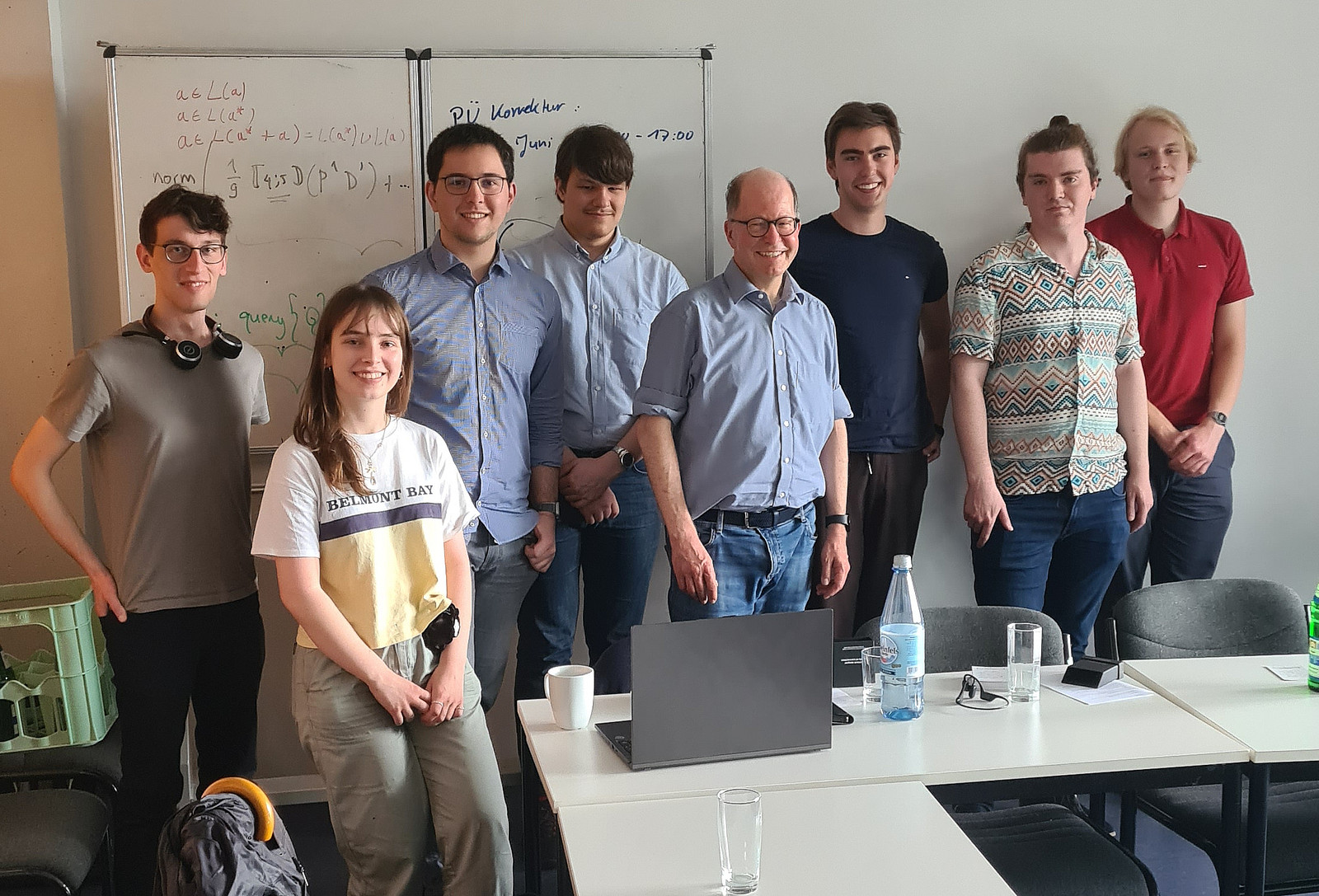 Eine Gruppe Studierender mit ihrem Professor stehen für ein Gruppenfoto in einem Seminarraum, sie lächeln