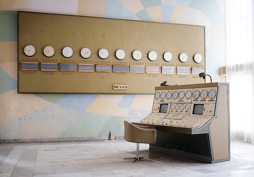 Das Foto zeigt eine leerstehende Kommandozentrale mit einem großen Pult im Vordergrund sowie einer Reihe von Uhren an der Wand dahinter. Der Raum wirkt wie aus einem vergangenen Jahrzehnt.