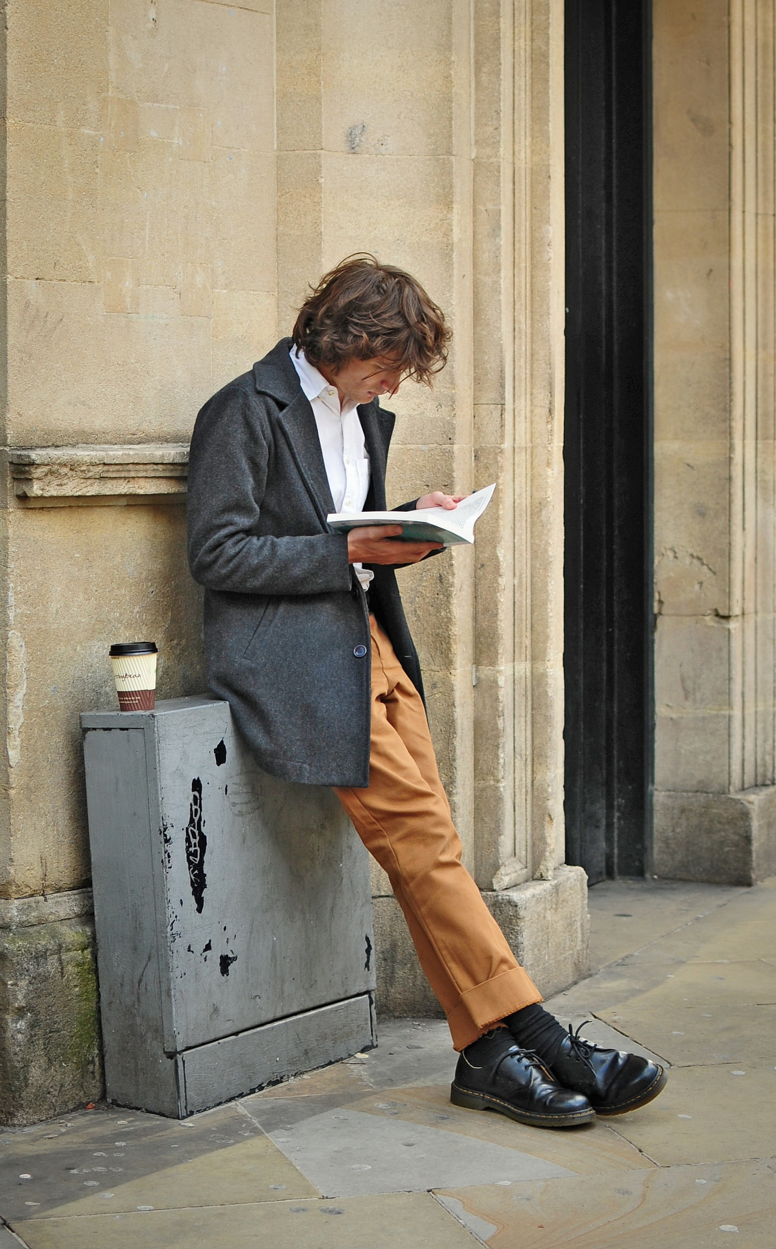 Ein Mann lehnt an einer Wand und liest ein Buch