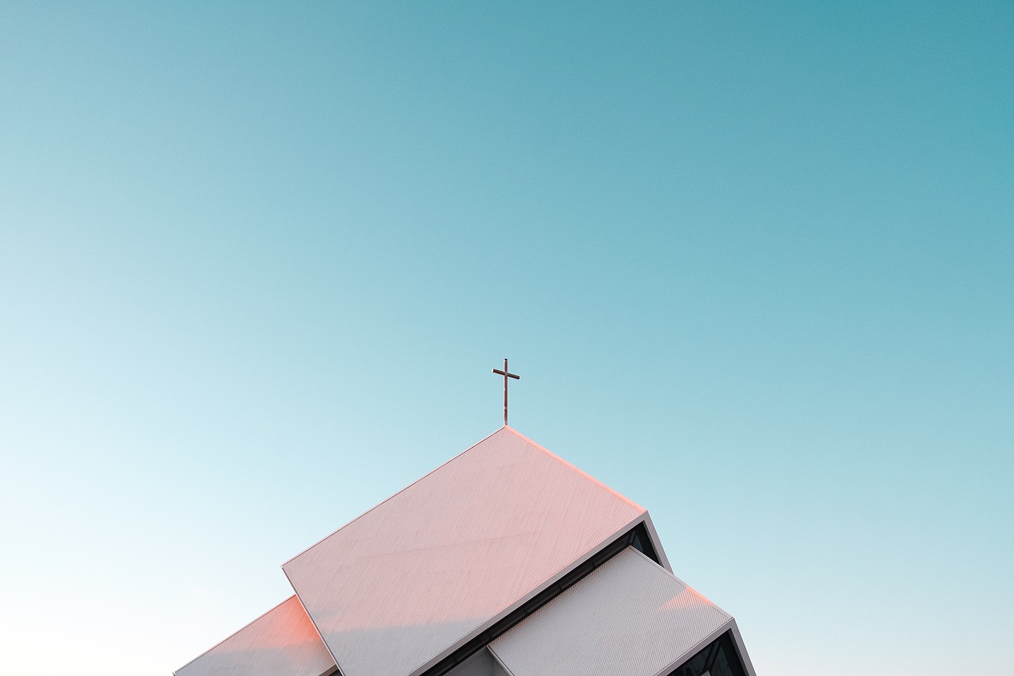 Dach einer modernen Kirche vor blauem Himmel, an der Spitze ein christliches Kreuz