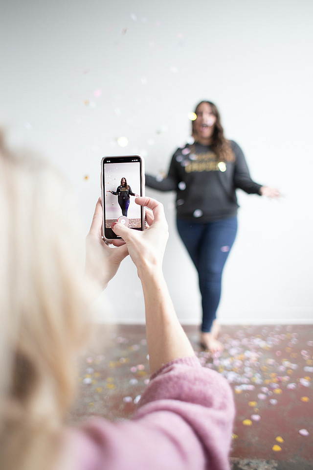 Eine Frau filmt mit der Tiktok-App auf ihrem Smartphone eine andere Frau, die im Konfettiregen tanzt