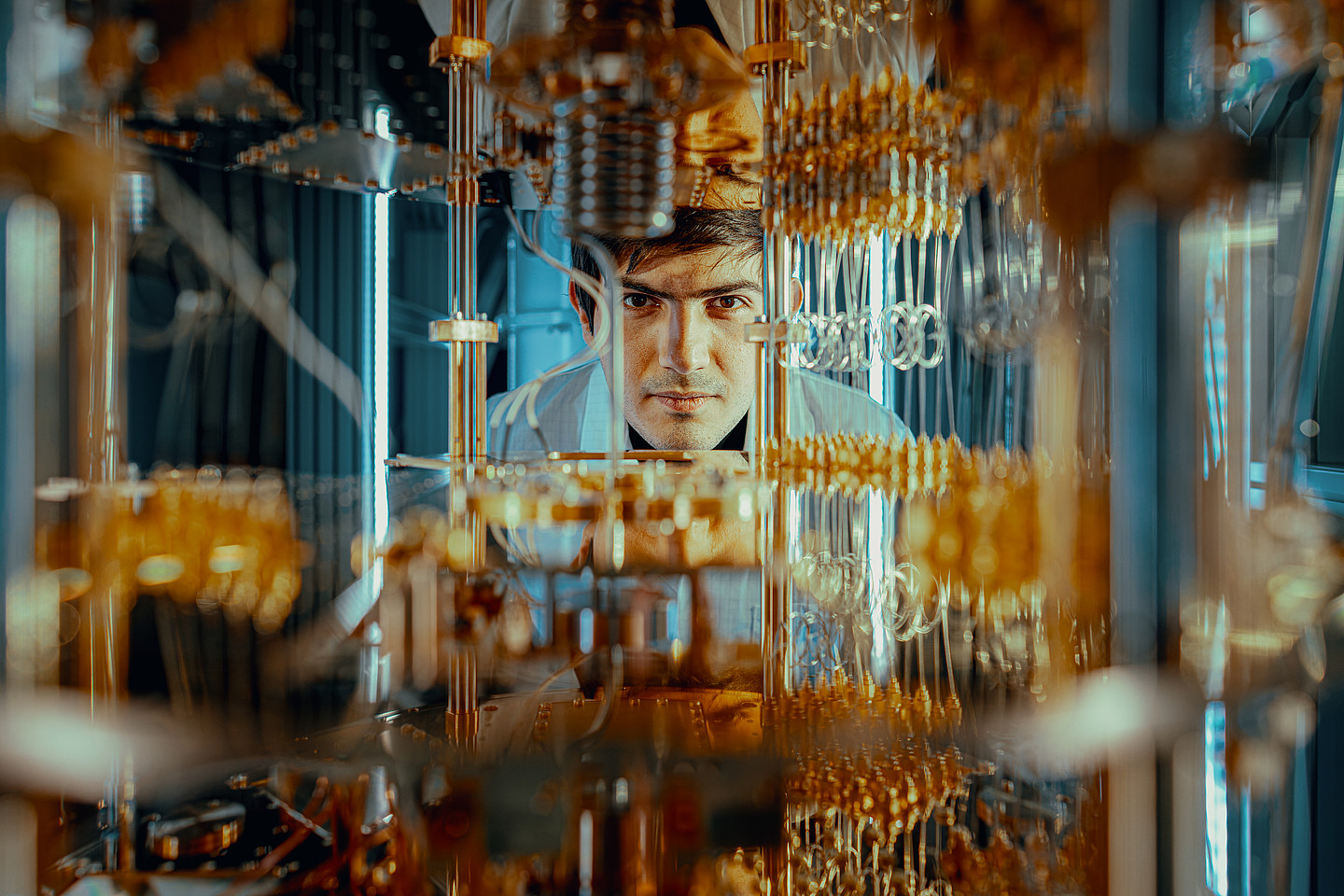 Ein Forscher, der durch Bauteile eines Quantencomputers hindurch in die Kamera blickt