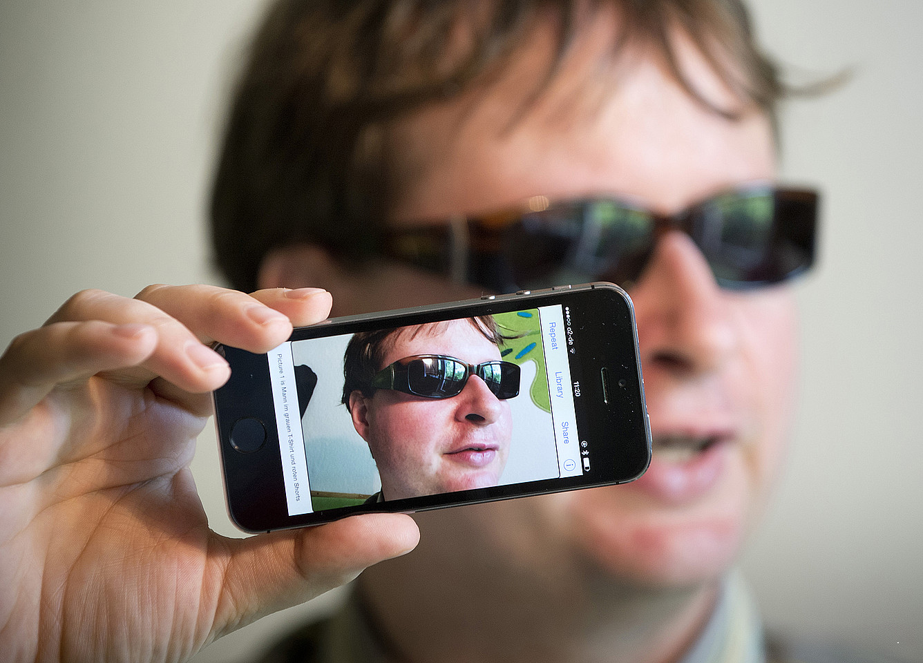 Porträt von Jan Blüher: Er trägt eine Sonnenbrille und hält ein Smartphone vor seinem Gesicht, auf dem dieses nochmals abgebildet ist.