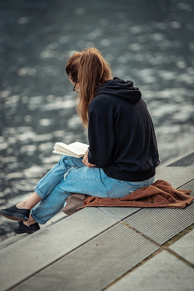 Eine Frau sitzt am Wasser und liest ein Buch
